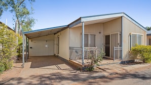A single-story building with a covered porch, a fenced outdoor area, and a small garden. - Karratha Caravan Park (Karratha Industrial Estate)
