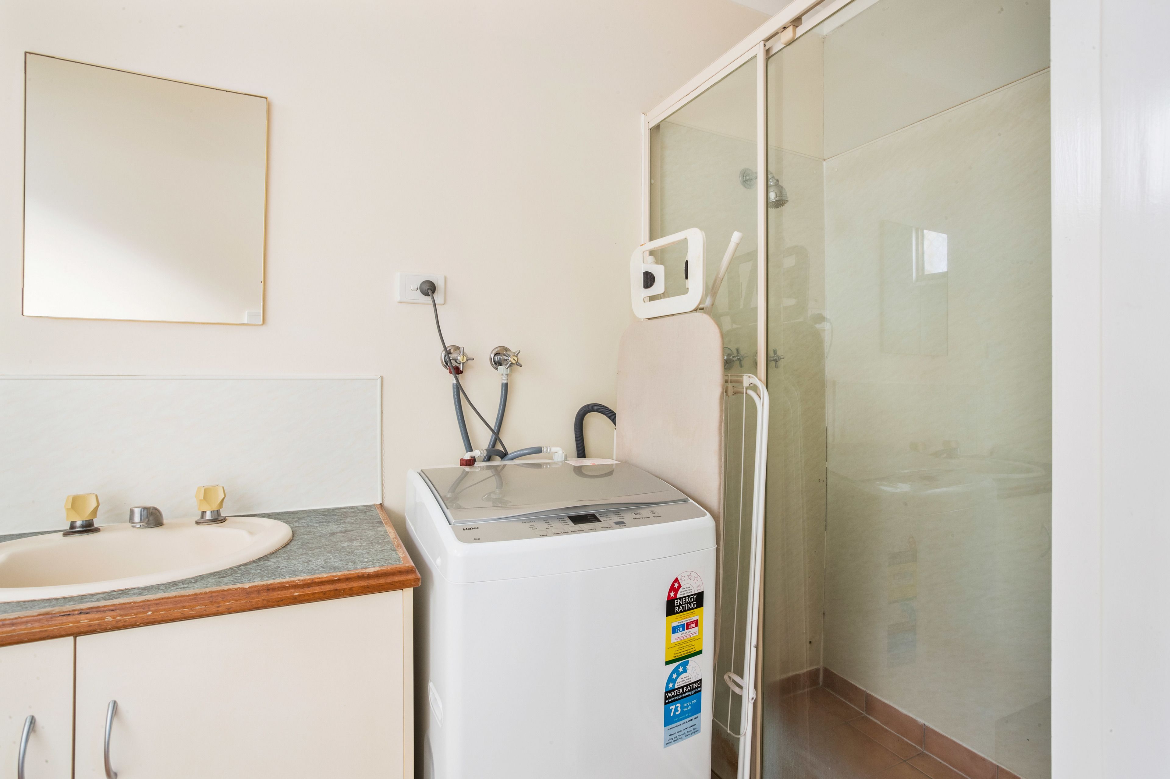 A bathroom with a sink, a washing machine, and a glass shower enclosure.