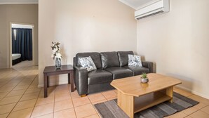 A modern living room with a leather sofa, a wooden coffee table, and a small side table with a vase of flowers. - Karratha Caravan Park (Karratha Industrial Estate)