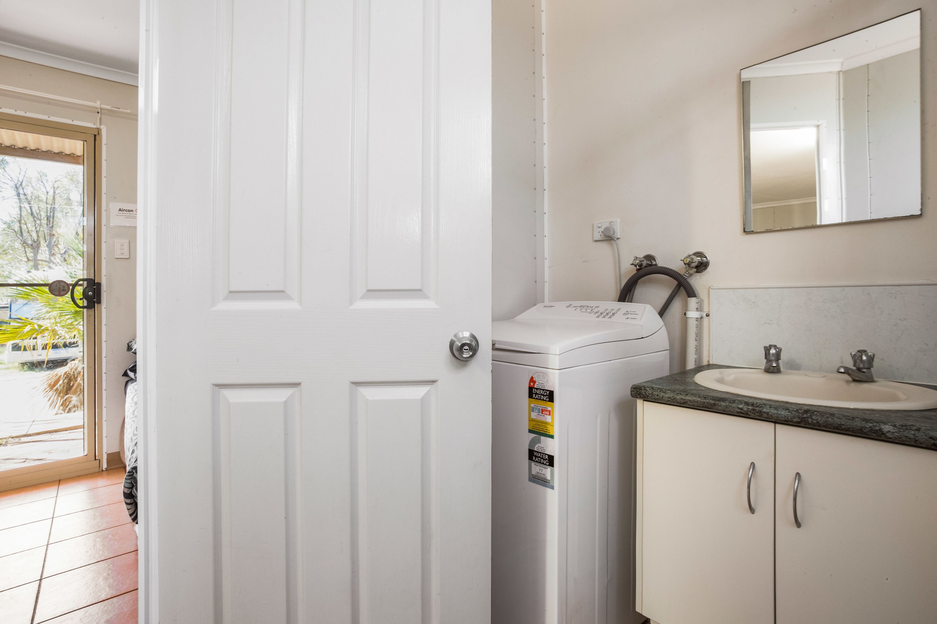Un baño con puerta blanca, lavadora, lavabo con espejo y vistas al exterior.