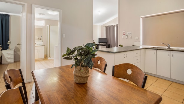 A modern kitchen with white cabinets, a wooden dining table, and a potted plant. - Karratha Caravan Park (Karratha Industrial Estate)