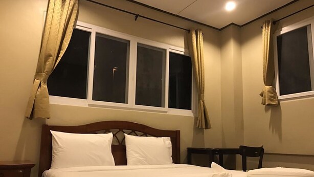 A hotel room with a bed, two windows, a nightstand, and a chair. - AN Apartment (Pattaya)