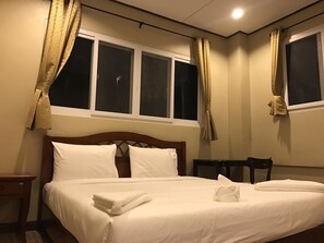 A hotel room with a bed, two windows, a nightstand, and a chair. - AN Apartment (Pattaya)