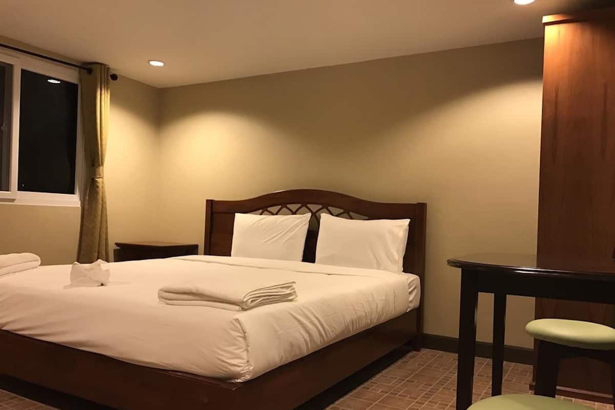 A neatly made bed with white linens and pillows, a wooden headboard, a small bedside table, and a chair with a cushioned seat.