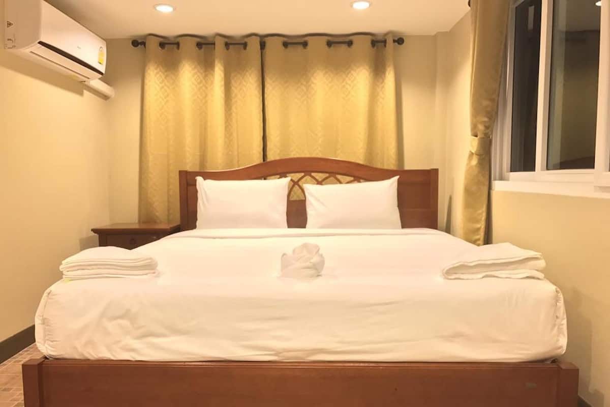 A neatly made bed with white linens, a wooden headboard, and a nightstand with a lamp.
