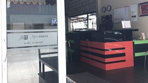 A reception area with a glass door, a counter with a red and black design, and a wall with a calendar and notices. - AN Apartment (Pattaya)