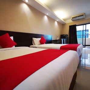 Quarto de hotel com duas camas, cada uma com roupa de cama vermelha e branca, cabeceira preta, uma pequena mesa com luminária e um aparelho de ar condicionado na parede.