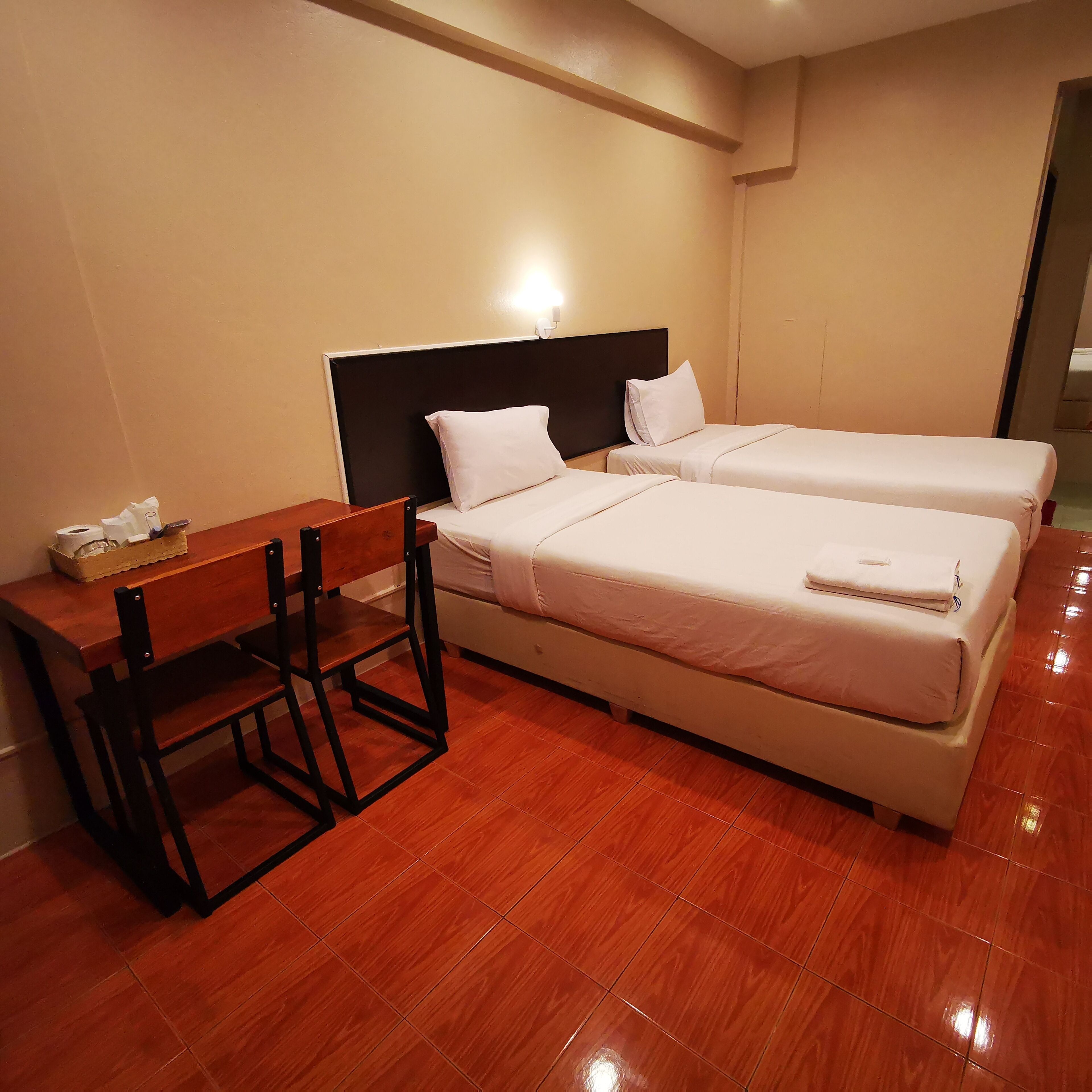 A hotel room with two beds, a wooden desk, and a chair.