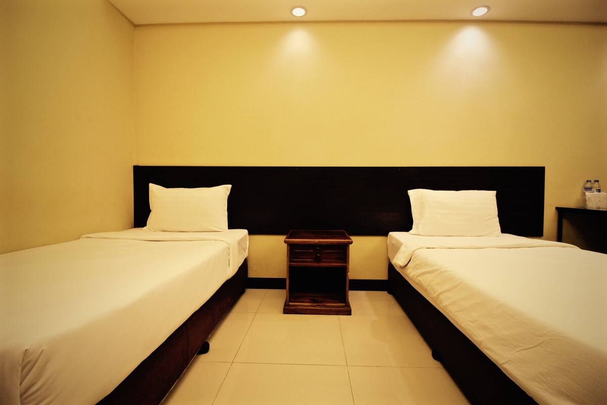 Une chambre d’hôtel avec deux lits simples, une table de chevet entre les deux et une petite table avec une lampe.