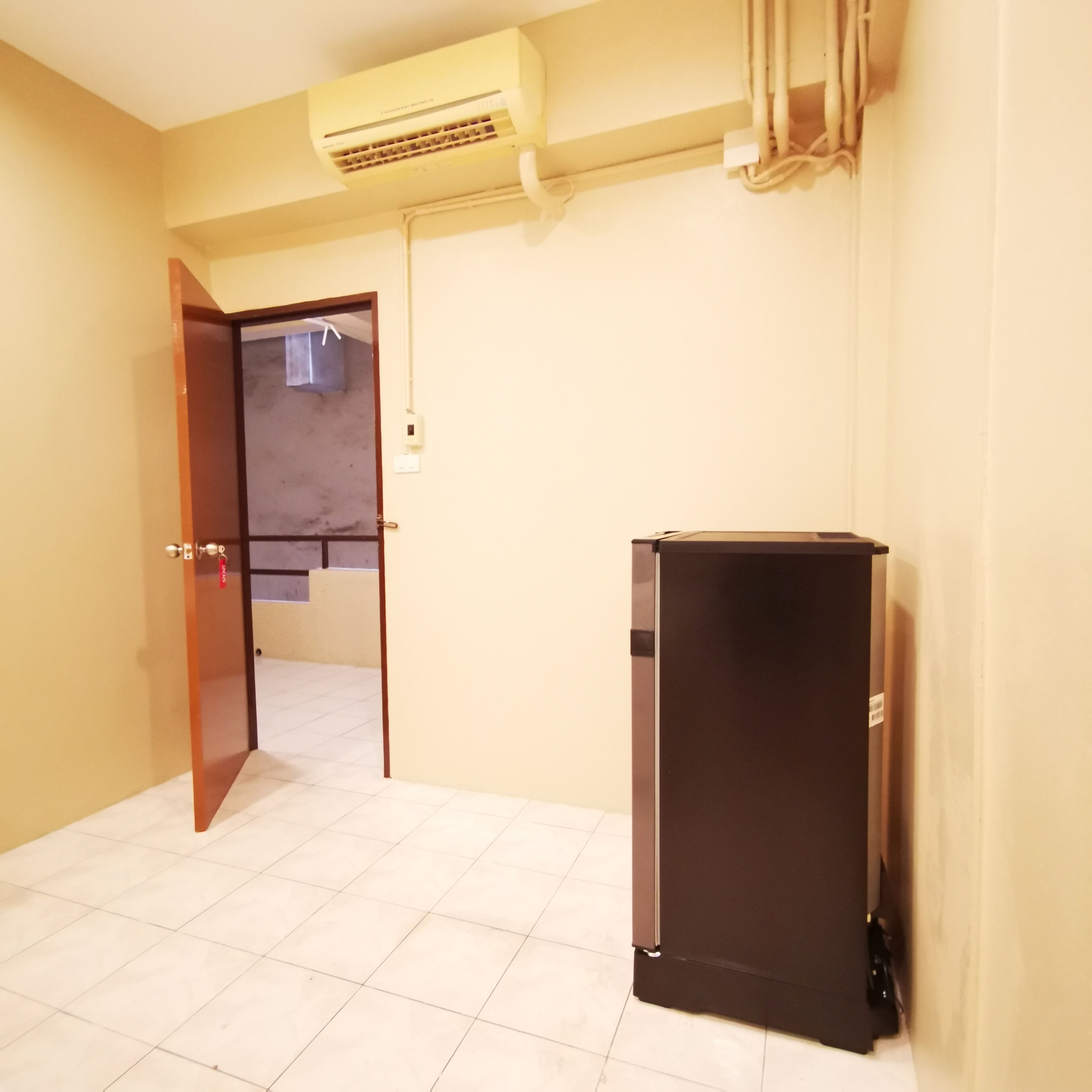 Una habitación con suelo de baldosas, un refrigerador negro y una puerta que da a otra habitación.