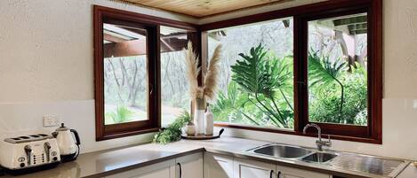 A kitchen with white cabinets, a stainless steel sink, a toaster, and a window with a view of greenery.
