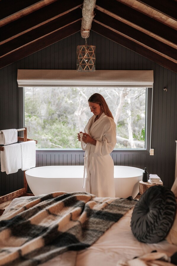 Una habitación con un ventanal grande, una bañera y una cama con manta.