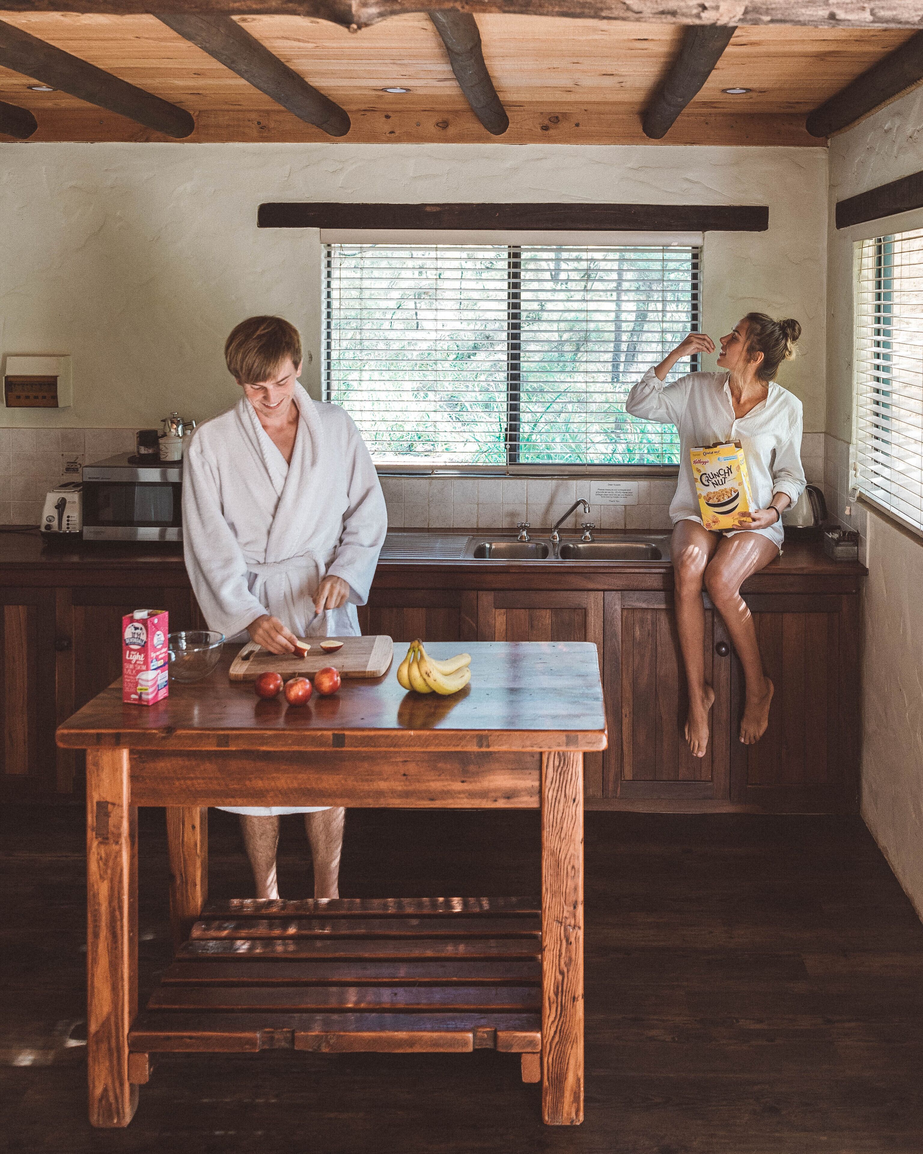 A kitchen with wooden cabinets, a wooden table, and a window with blinds.