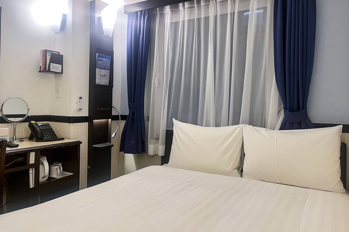Une chambre d’hôtel comprenant un lit, un bureau avec un téléphone, un miroir et une étagère avec une bouilloire et des tasses.