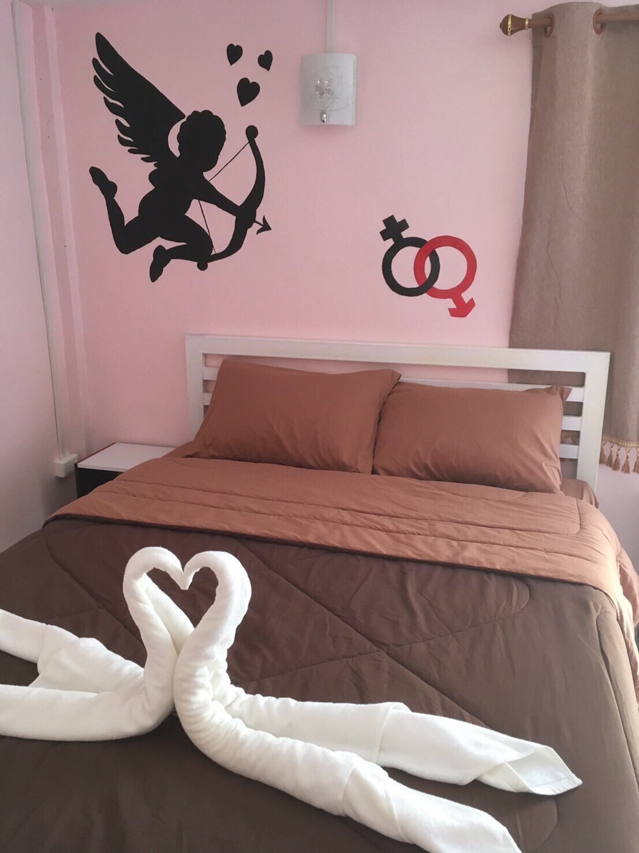 A bedroom with a pink wall, a white bed frame, brown bedding, and decorative swans on the bed.