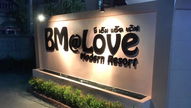 Letrero para BMOLove Modern Resort con texto iluminado y una maceta con follaje al frente.