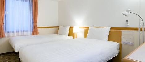 A hotel room with two single beds, a bedside table with a lamp, a window with sheer curtains, and a wall-mounted control panel.