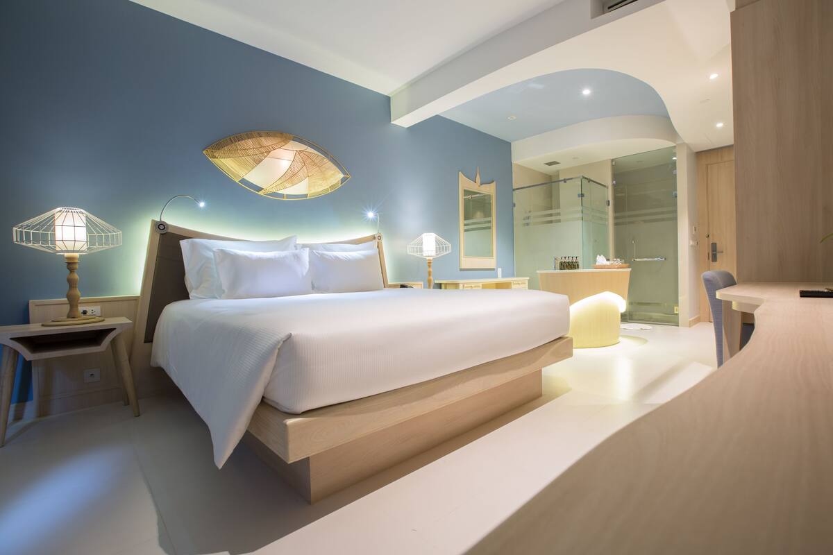 Un dormitorio moderno con una cama grande, lámparas de noche, un espejo y un baño visible a través de una puerta de cristal.