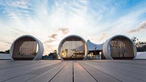 A modern architectural structure with three large circular openings, a wooden deck, and a clear sky.