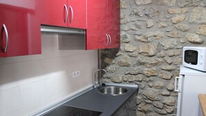 A kitchen with red cabinets, a stone wall, a stainless steel sink, and a microwave. - Mountain apartment (SORT)