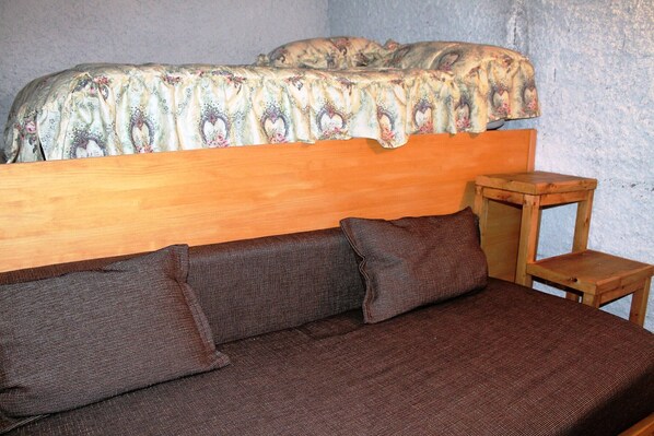 A bed with a floral bedspread, a wooden headboard, and a small wooden nightstand with a pillow. - Mountain apartment (SORT)