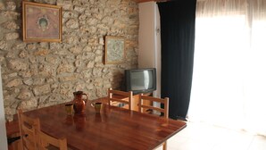 A dining area with a stone wall, wooden ceiling, a TV, and a table with chairs. - Mountain apartment (SORT)