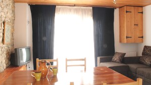 A room with a wooden table, chairs, a television, a sofa, and a cabinet. - Mountain apartment (SORT)