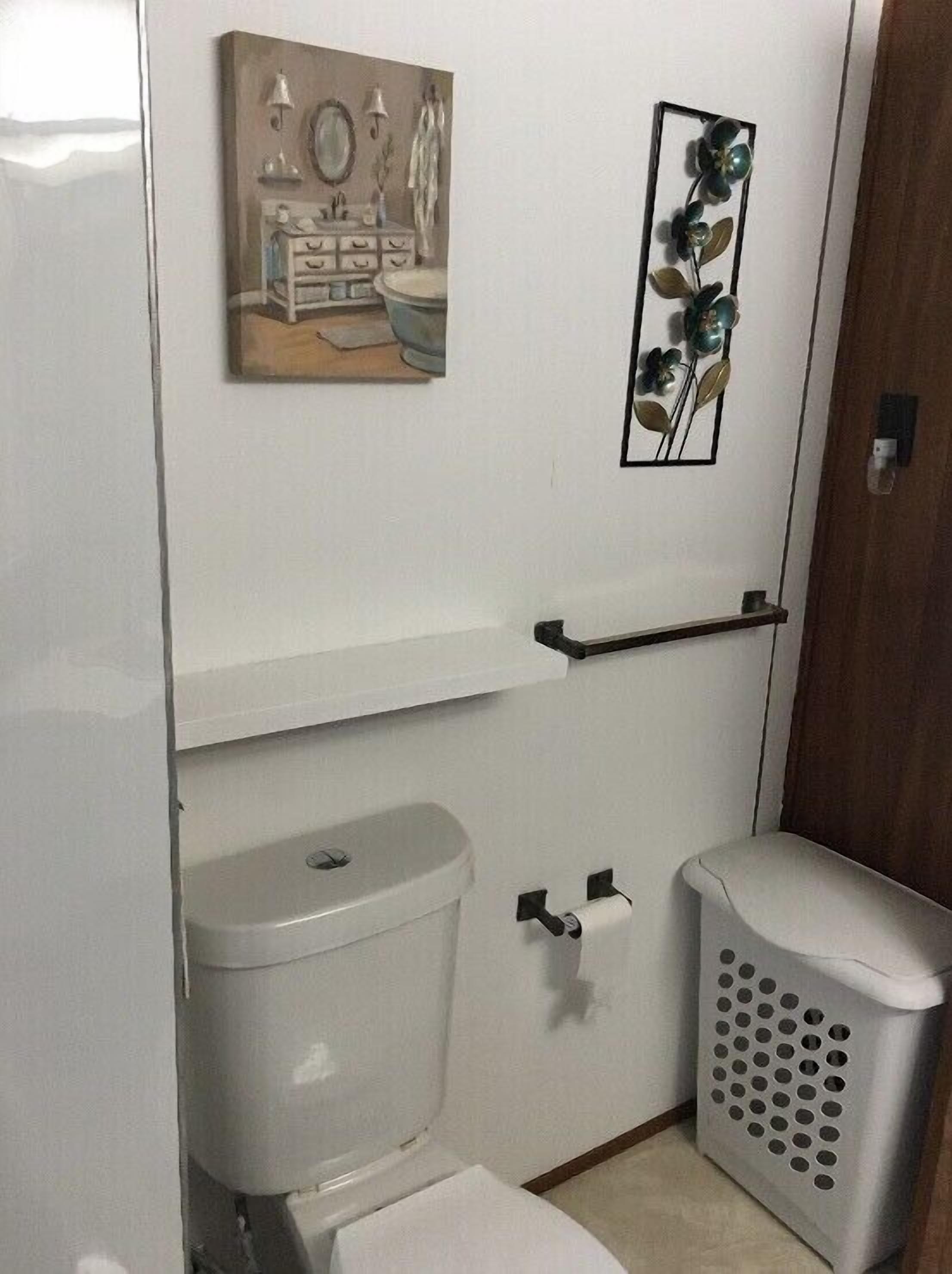 A small bathroom with a toilet, a sink, and a shelf above the toilet.