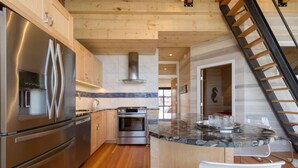 A modern kitchen with stainless steel appliances, wooden cabinets, a granite countertop, and a visible staircase. - Old Port Penthouse Suite - Amazing Harbor Views (Portland)