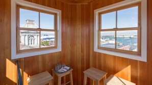 A room with wooden paneling, two windows with a view of a cityscape and water, and a small table with glasses and a tray. - Old Port Penthouse Suite - Amazing Harbor Views (Portland)