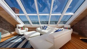 A modern loft bedroom with a sloped ceiling, large skylight windows, and a view of the cityscape. - Old Port Penthouse Suite - Amazing Harbor Views (Portland)