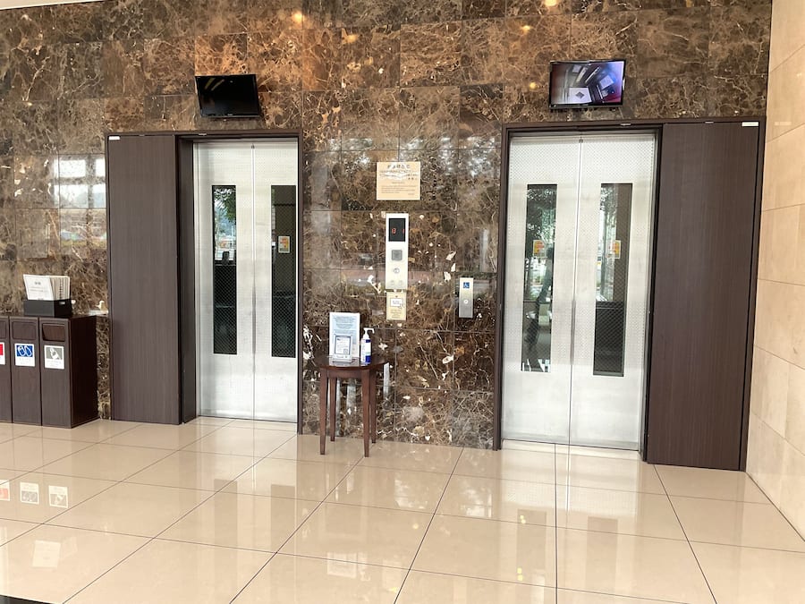 A lobby with two elevators, a reception desk, and a digital display.