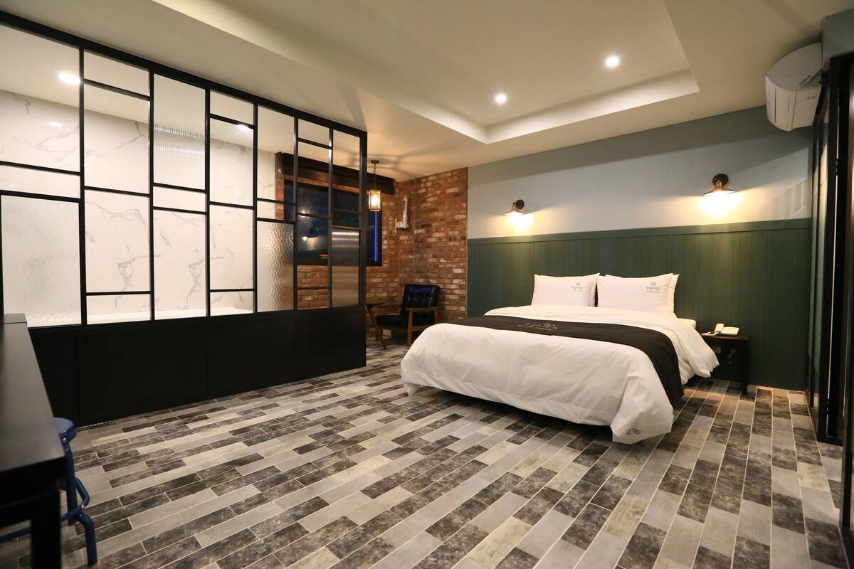 A hotel room with a large bed, a desk, a chair, and a partition with frosted glass panels.