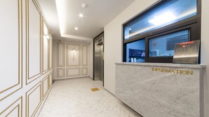 Et receptionsområde med en marmordisk med skiltet "INFORMATION", en moderne elevator og et fiskebensmønstret gulv.