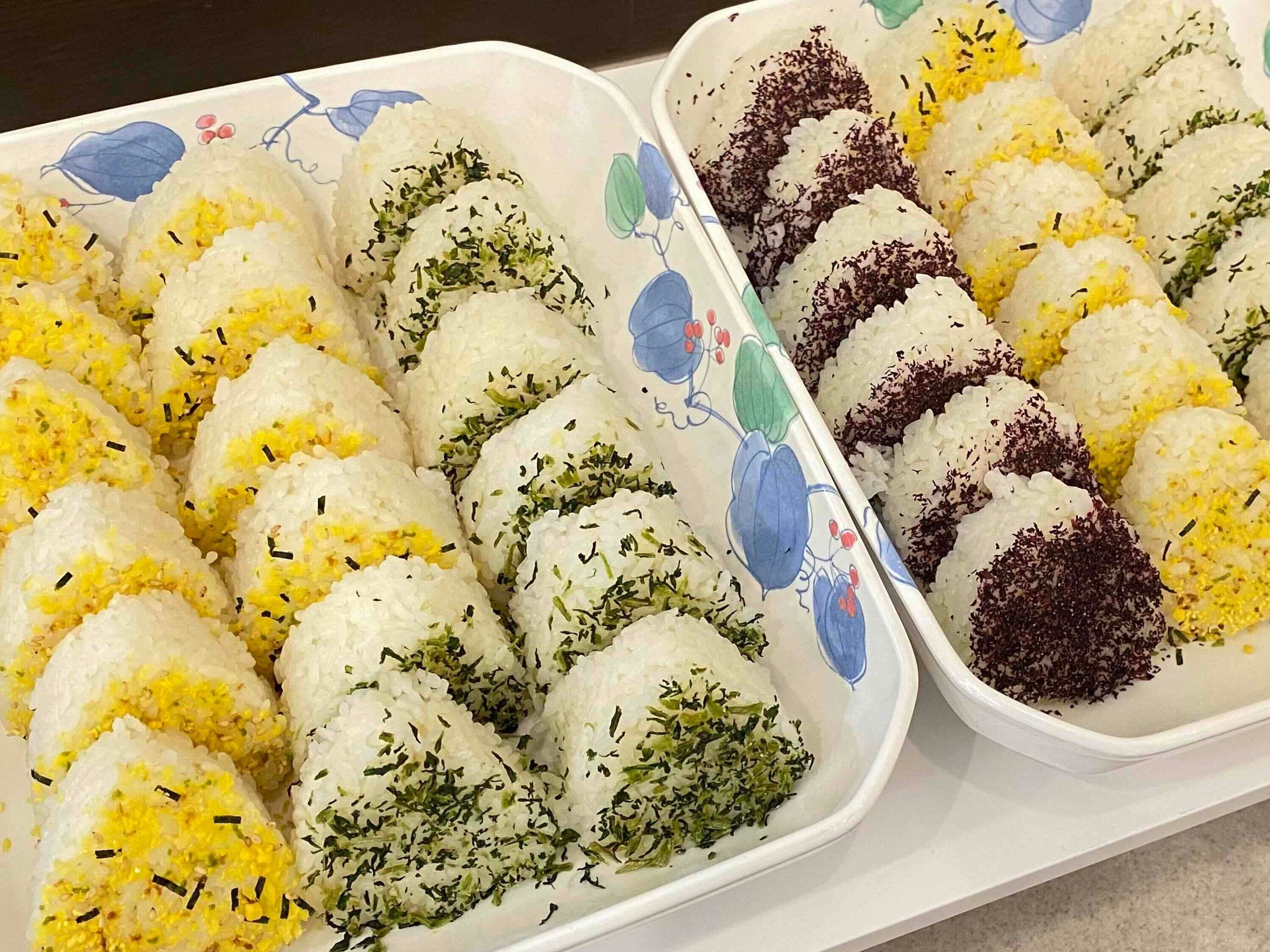 Een dienblad met rijstballen, waarvan sommige gele en andere groene toppings hebben.