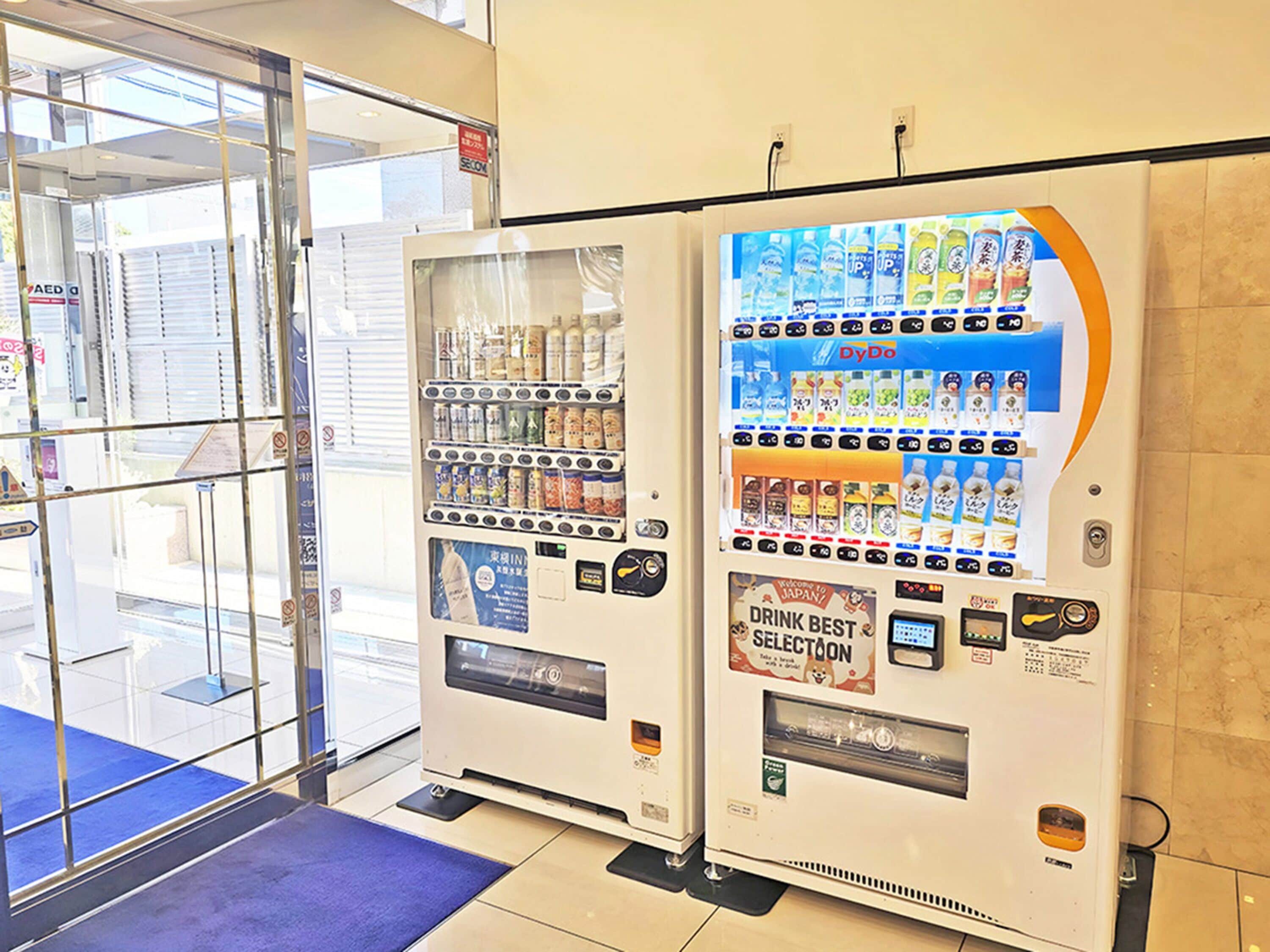 Two vending machines inside a building with a glass door and a blue carpet.