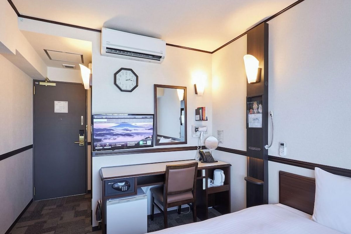 Une chambre d’hôtel équipée d’un lit, d’un bureau, d’une chaise et d’un téléviseur diffusant un paysage de montagne.