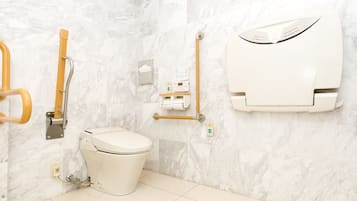 Casa de banho moderna com sanita, barras de apoio, secador de mãos e dispensador de papel.