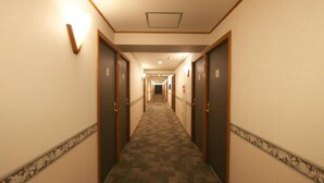 A hotel corridor with carpeted floors, wooden doors, and wall-mounted light fixtures. - Toyoko Inn Tsu-eki Nishi-guchi (Tsu)
