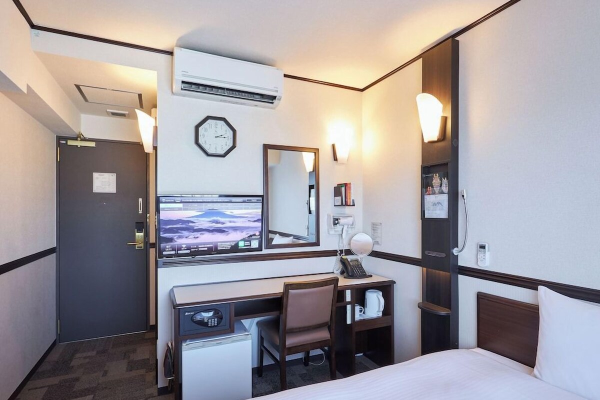 Une chambre d’hôtel équipée d’un lit, d’un bureau, d’une chaise et d’un téléviseur diffusant un paysage de montagne.