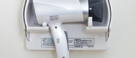 A hair dryer mounted on a wall with a power cord plugged in.