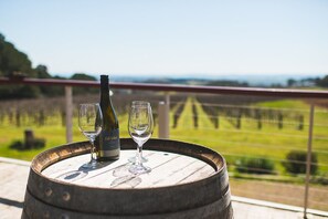 A wooden barrel with a wine bottle and two glasses on a balcony overlooking a vineyard. - The Sampson - Orange (Orange)