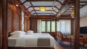Une chambre traditionnelle en bois, dotée d’un grand lit, de meubles en bois et offrant une vue sur la verdure environnante.