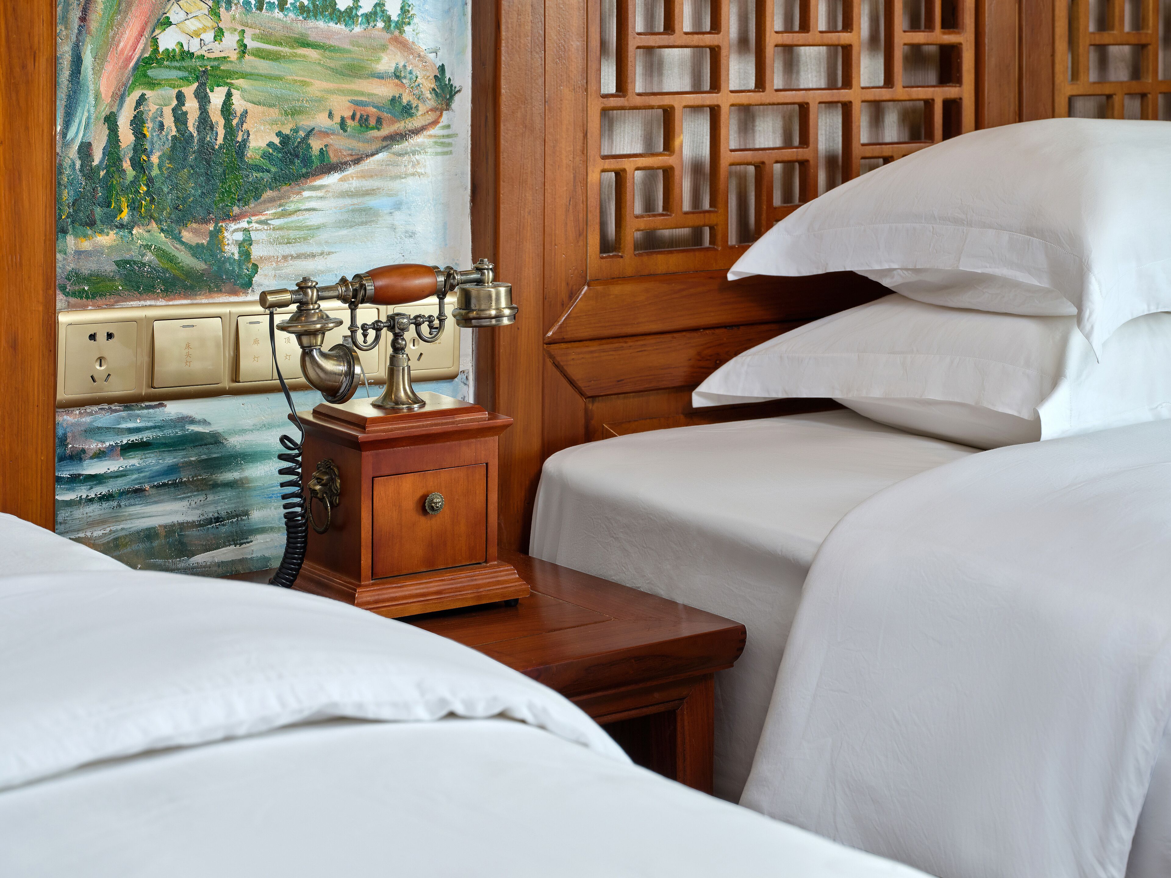 Habitación de hotel con cabecera de madera, un cuadro de un paisaje y un teléfono antiguo.