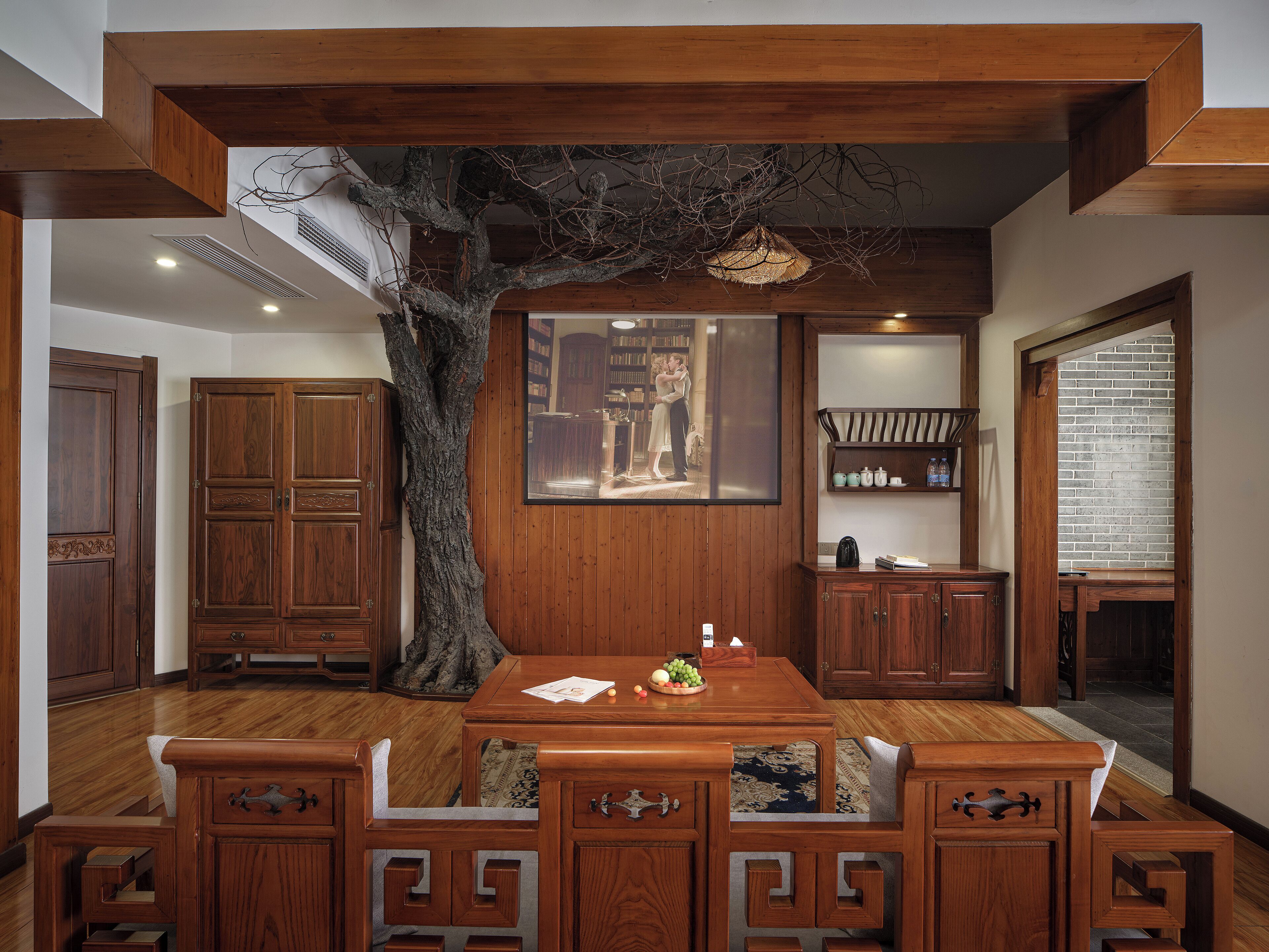 A dining area with a wooden table and benches, a large tree sculpture, and a framed picture on the wall.