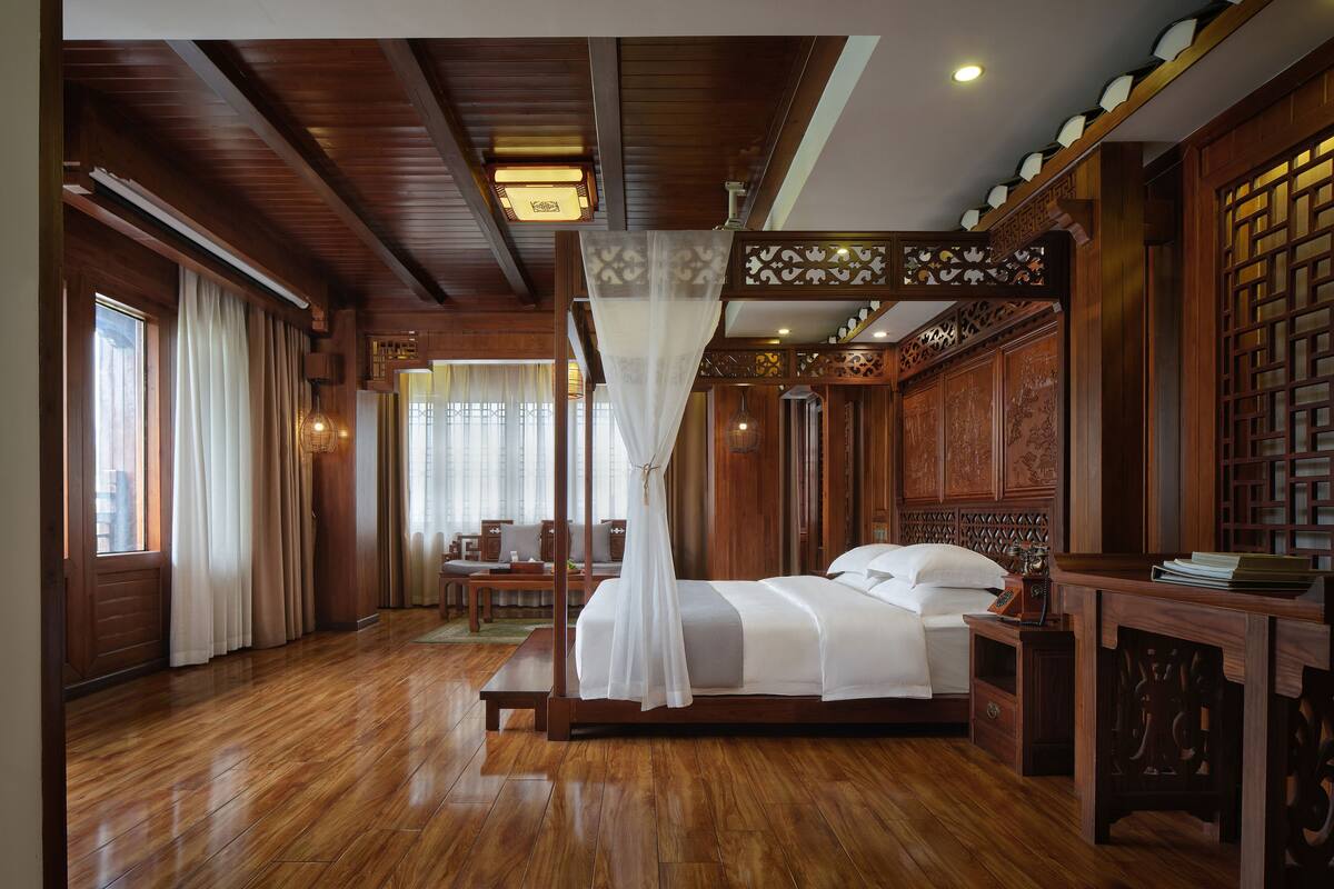 Un dormitorio de madera tradicional con cama de dos columnas, un escritorio de madera y vistas al exterior a través de una ventana.