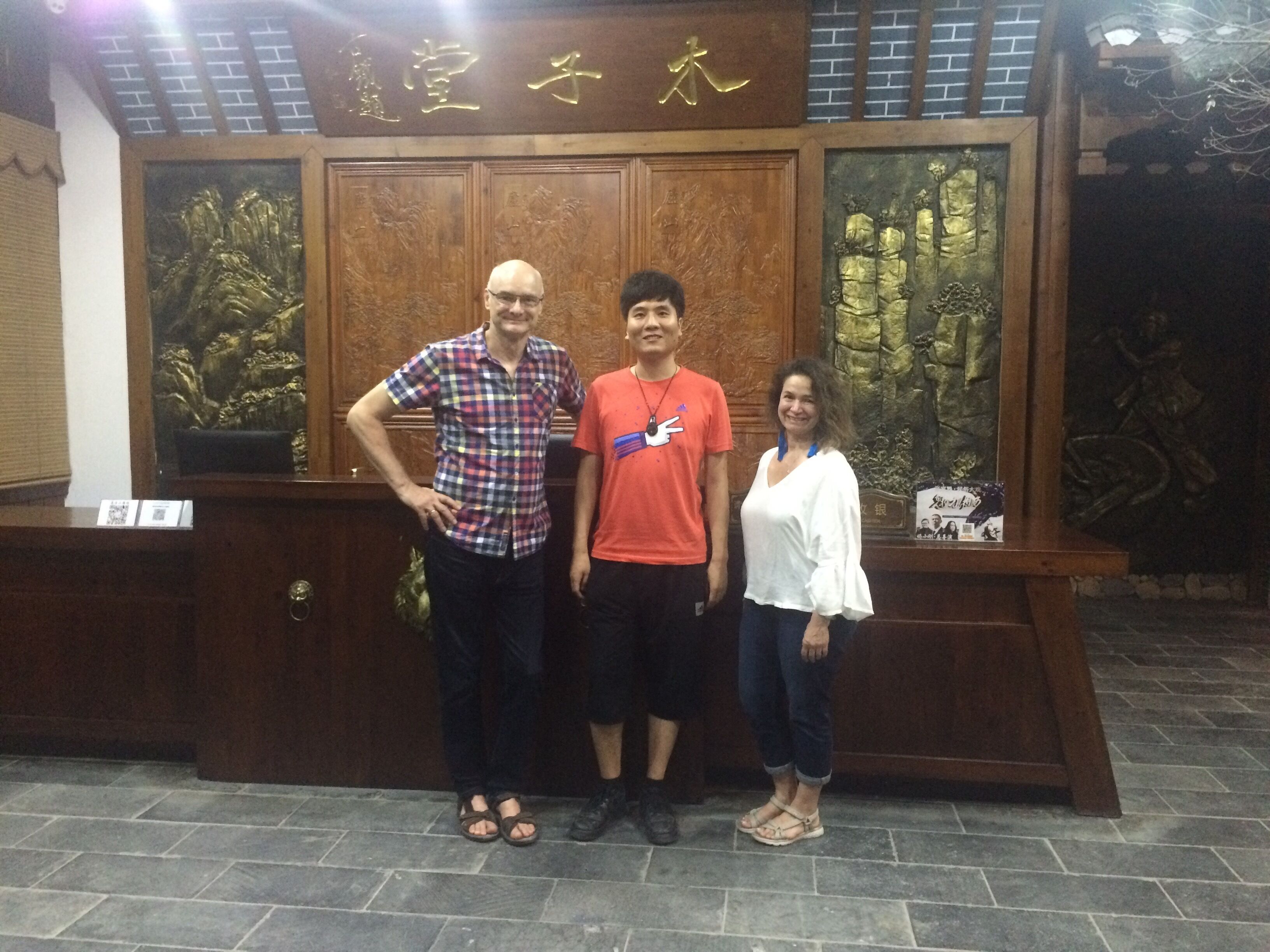 Three people standing in front of a wooden panel with intricate carvings and a plaque.