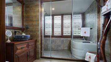 A bathroom with a wooden vanity, a round mirror, a white sink with a decorative bowl, a large mirror above the vanity, a shower with a glass door, and a towel rack with a towel.