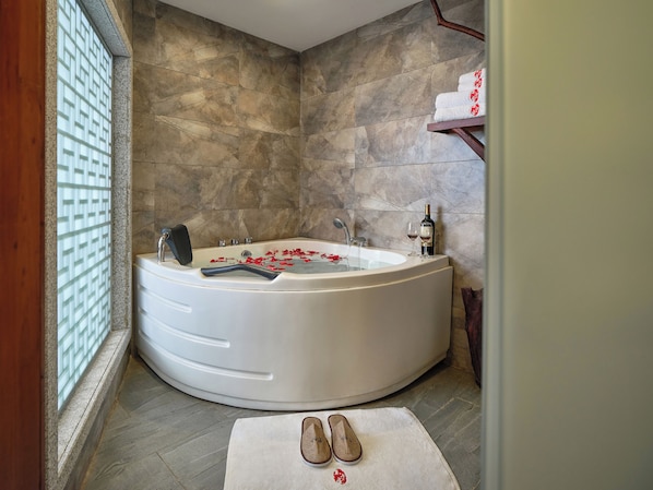 Une salle de bain moderne avec une baignoire sur pieds, une étagère en bois où sont posées des serviettes et une paire de chaussons sur un tapis.
