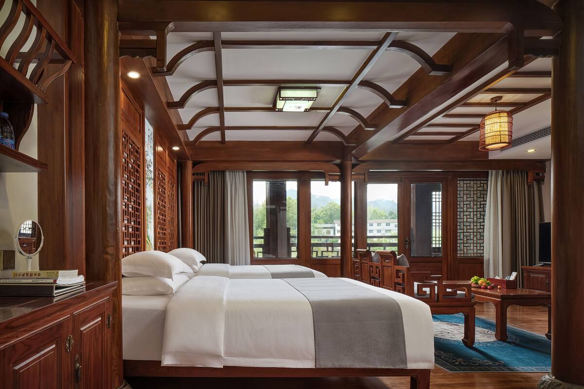 Una habitación tradicional de madera con una cama grande, un escritorio de madera y vistas al exterior a través de amplios ventanales.